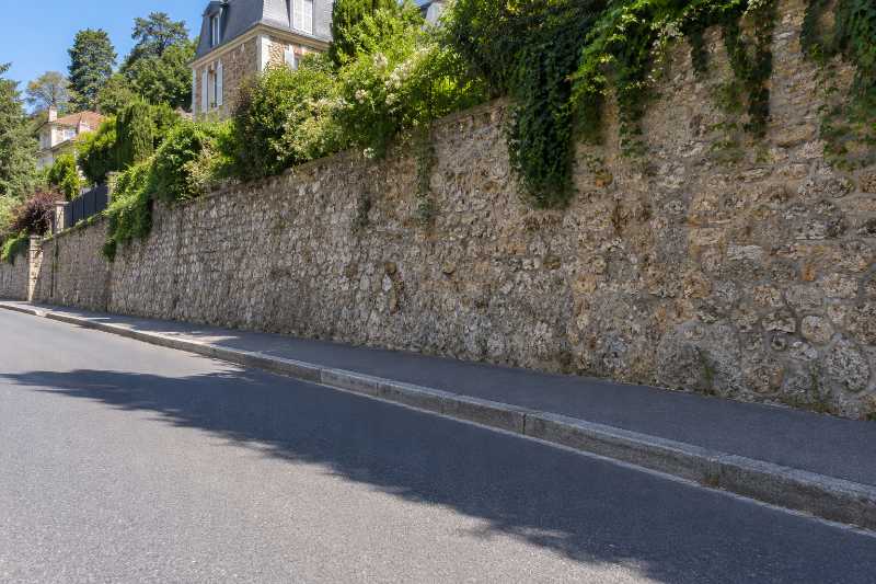 Bande de trottoir et de chaussée laissée libre au pied d'un mur de soutènement