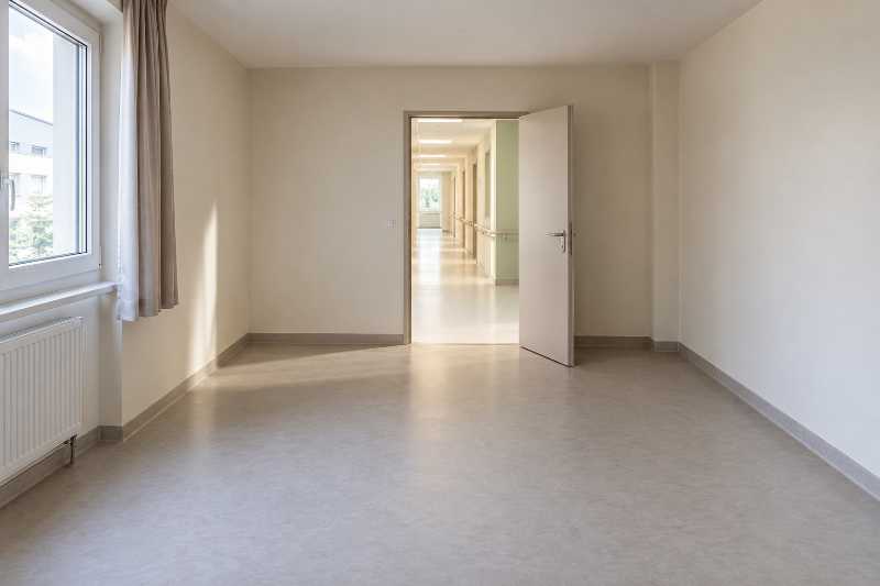 Chambre d'établissement entièrement vide, vue depuis le fond vers la porte ouverte