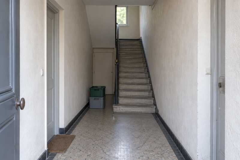 Hall étroit d'un petit immeuble, première volée d'escalier sans ascenseur