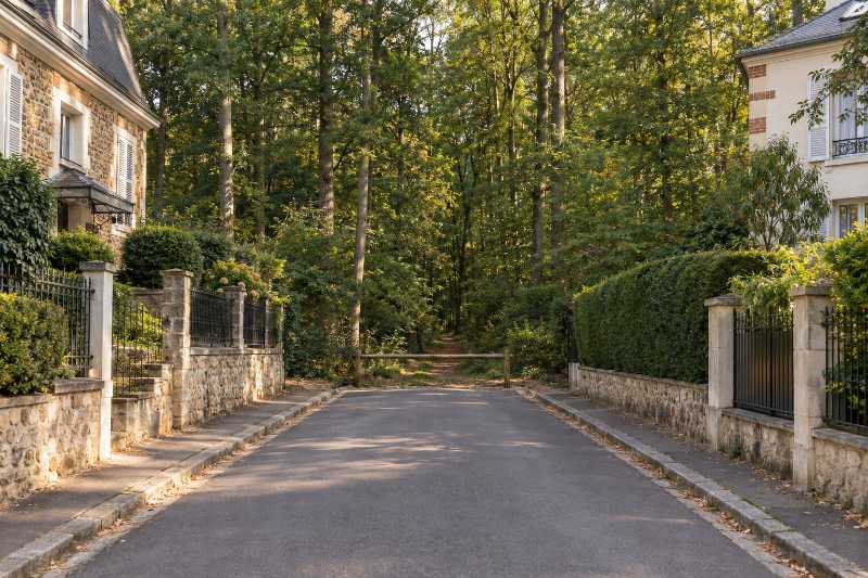 Rue résidentielle se terminant sur la lisière de la forêt, chemin forestier au fond