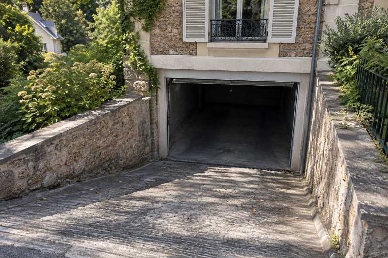 Rampe bétonnée descendant vers un garage en demi-sous-sol sous une villa de coteau